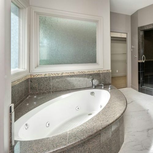 Spacious white and gray bathroom with jacuzzi tub by windows in Encino, California