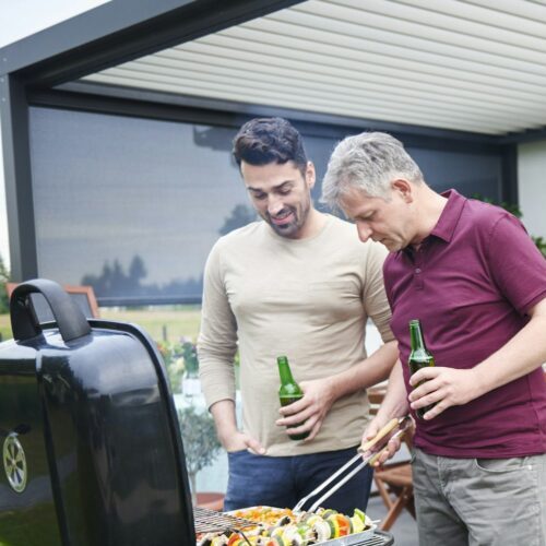 Mature and mid adult man barbecuing at family lunch on patio