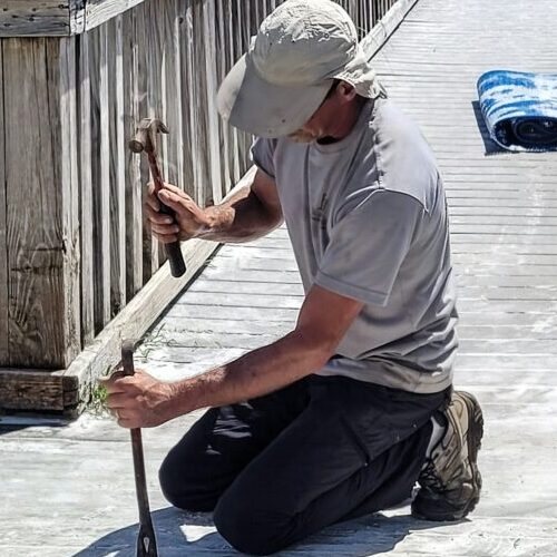 Young millennial working on beach walkway with hammer and claw removal of wood planks.